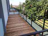 Balkon mit Boden aus Holzbohlen und Stahlgeländern mit Glasfüllung