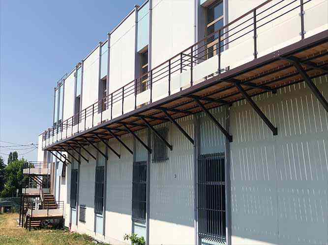 Balkon und Außentreppe mit Stützkonstruktionen aus verzinktem und pulverbeschichtetem Stahl, Holzbohlen und Geländern mit Glasfüllung
