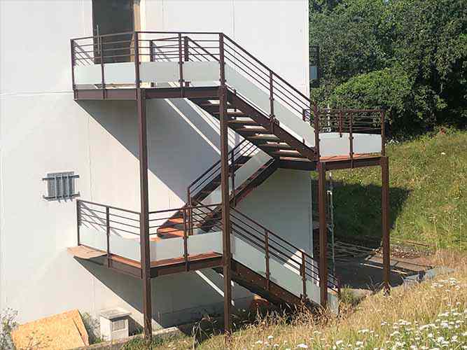 Außentreppen aus Stahl und Holz mit Glasgeländer.